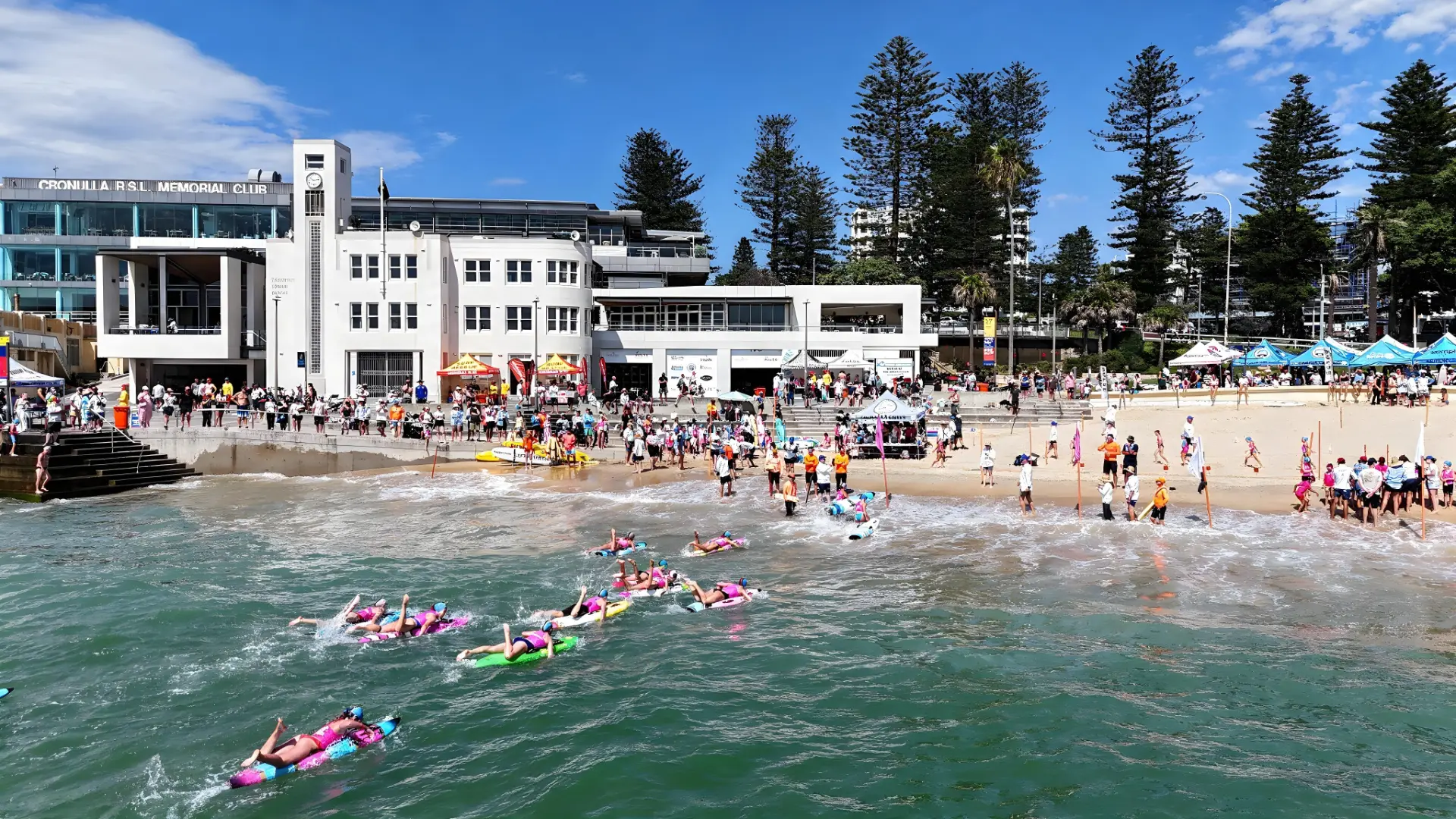 Crowds at Cronulla Beach in front of the club for a Nipper carnival, with young competitors paddling out into the water